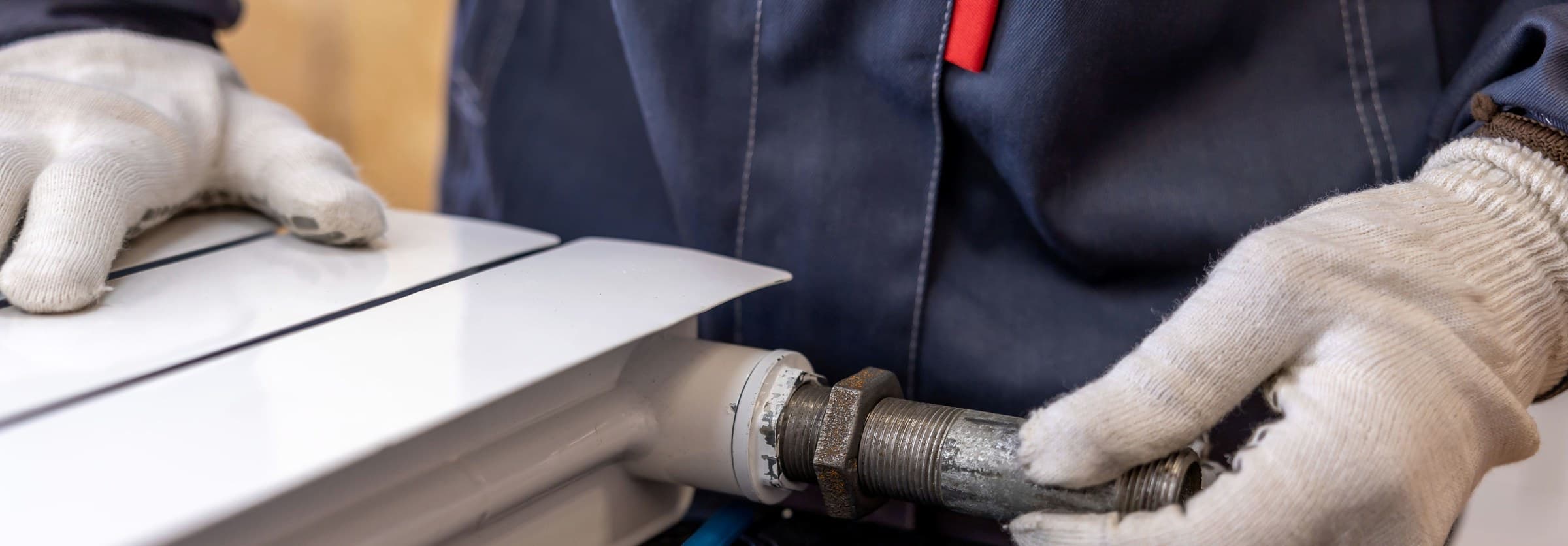 A plumber's gloved hands fitting a threaded supply pipe during an install