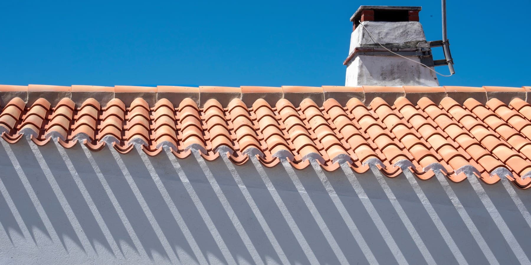A finished barrel tile roof and chimney under a clear sky