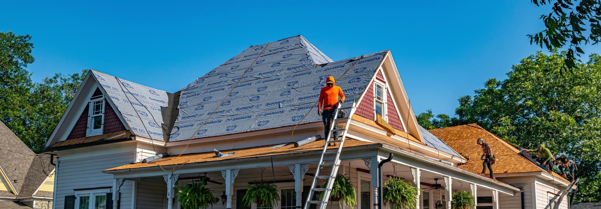 A roofing crew replacing the full roof of a two-story home, ladder against the eave