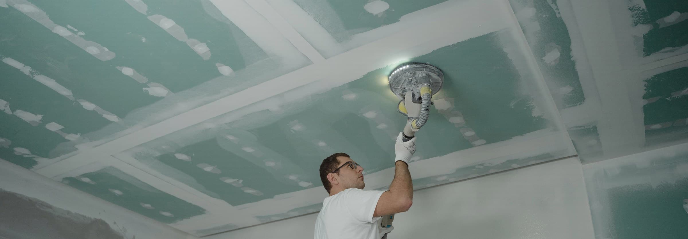 A worker sanding a repaired drywall ceiling, the rebuild stage after water damage